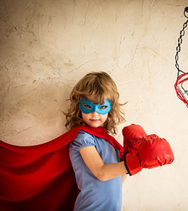 Superhero kid in red boxing gloves punching on the drawn bag. Winner and success concept