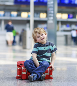 Blond boy of 2 years sitting on suitcase at the airport, indoors and waiting for going on vacations.